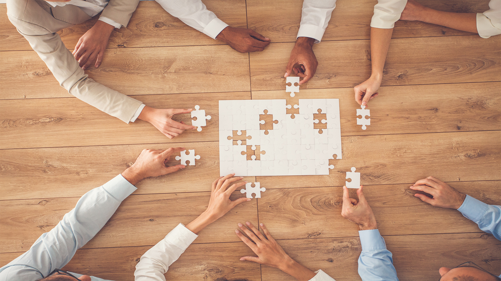 Hands assembling a puzzle on a wooden table. Concept of teamwork and collaboration.