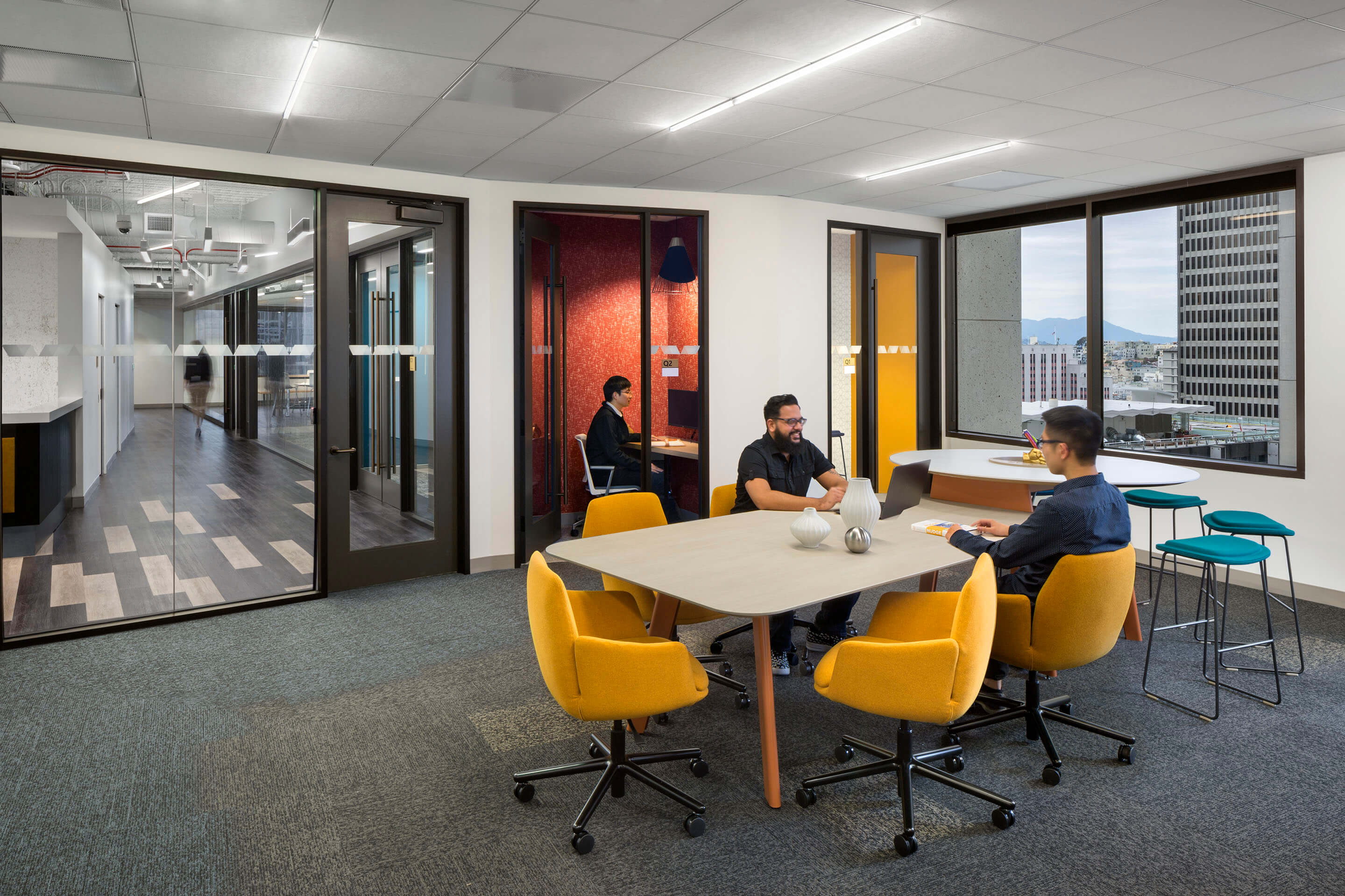 People sitting around a table in an office space. Building view through a window.