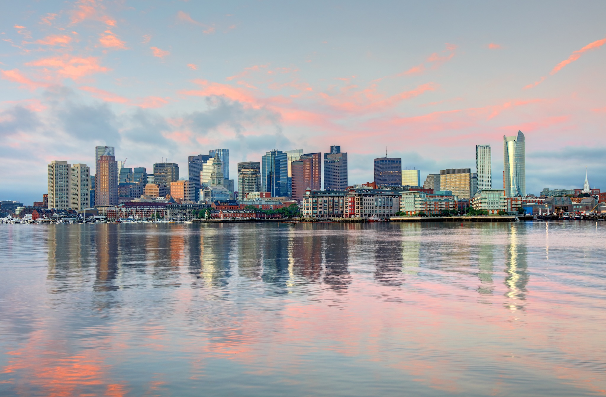 Boston skyline reflecting in water under a pink sky.