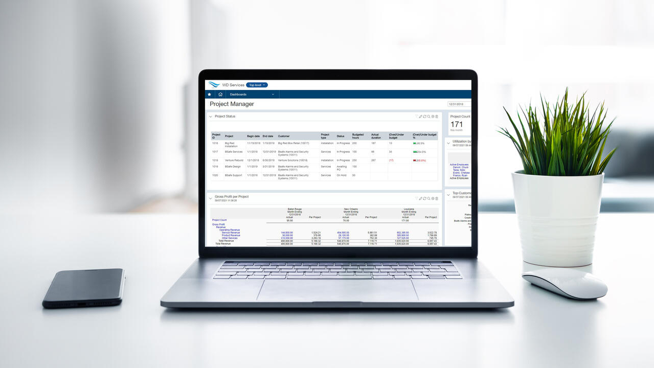 Laptop on a desk displaying the project manager screen, beside a potted plant, mouse, and phone.
