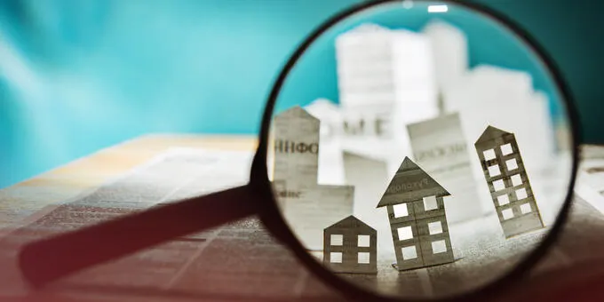 Magnifying glass over paper houses. Focus on detail.