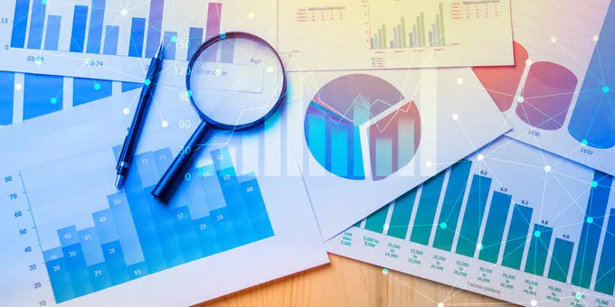 Charts, magnifying glass, and pen on desk; business analysis concept.