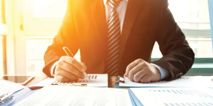 Person working on documents at desk with pen and graphs.