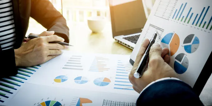 Two people analyzing business data, pie and bar charts.