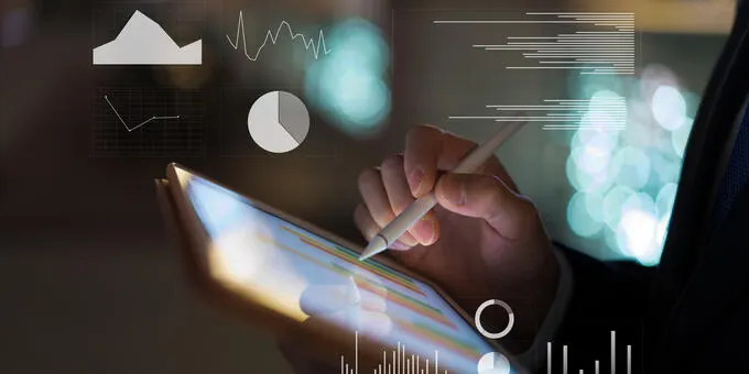 Person uses stylus on tablet displaying financial charts. Bokeh background.