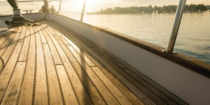 Wooden boat deck with water and landscape in background. Golden hour sunlight.