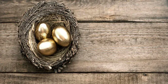 Three gold eggs in a nest on a wooden surface.