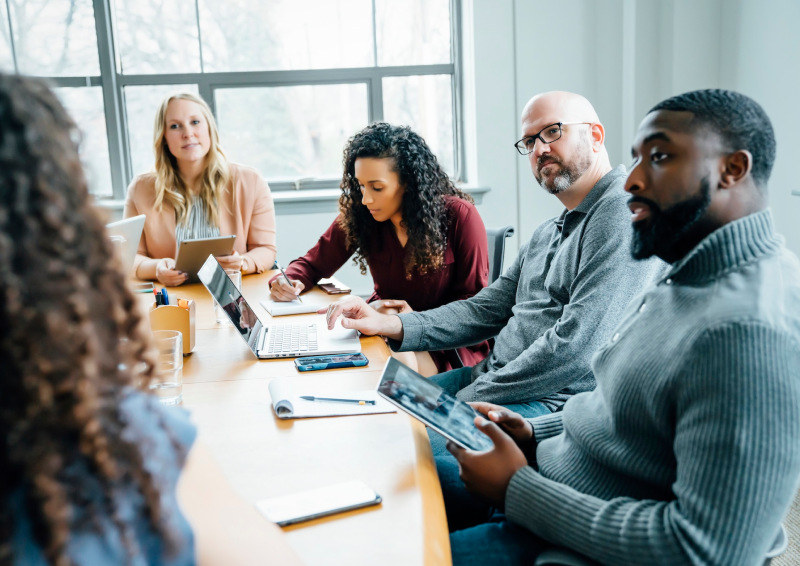 Group of people sitting around a table, using technology and taking notes.