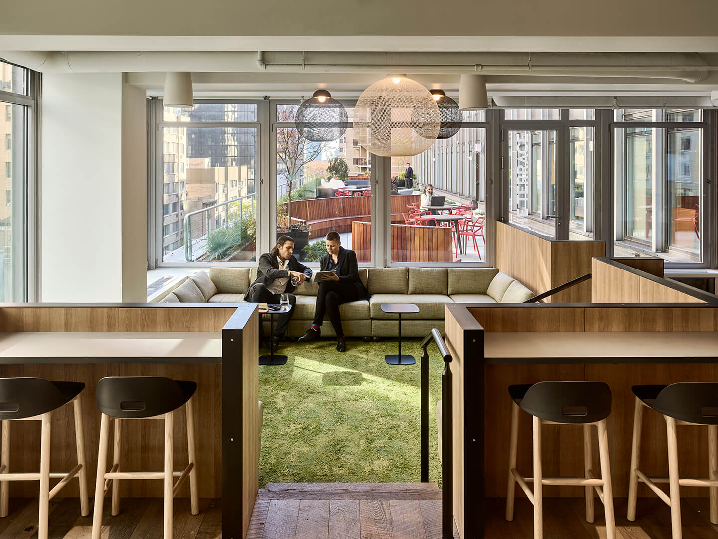 Two businesspeople in an office lounge area with a view of a terrace.