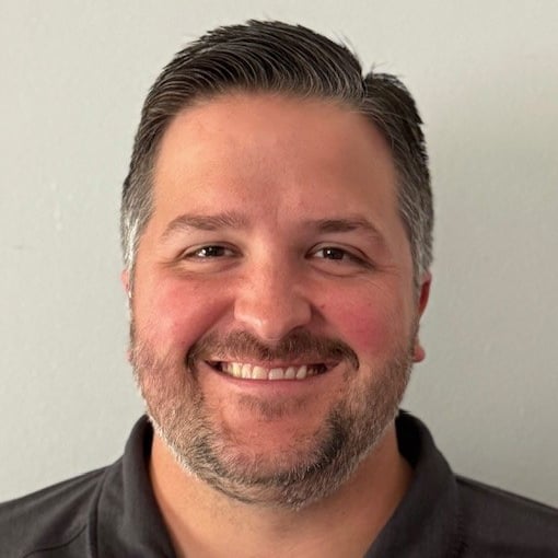 Portrait of a smiling man with a beard, wearing a dark gray polo shirt.