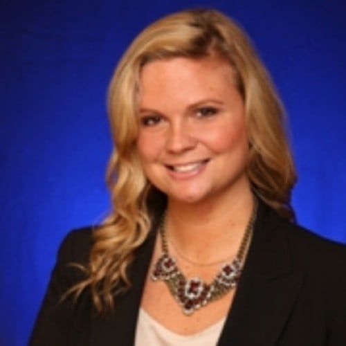 Woman with blonde hair smiles, wears a blazer and necklace.