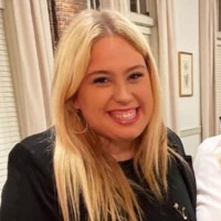 Blonde woman smiling, hoop earrings, black top.