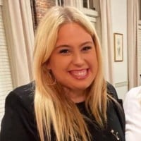Blonde woman smiling, hoop earrings, black top.