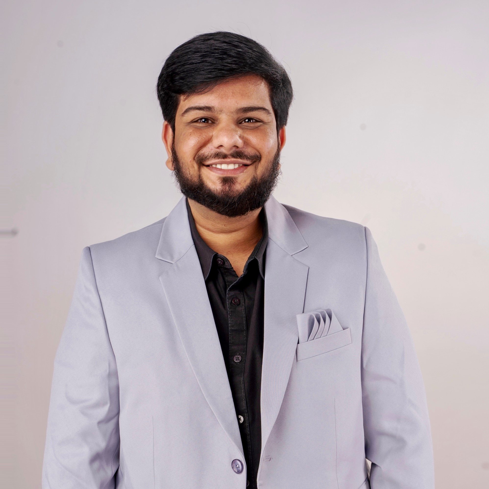 Man wearing a gray suit and a black shirt, smiling at the camera.