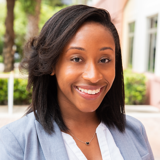 Headshot of Ruth Augustin wearing a blazer and smiling. She has a heart pendant necklace.