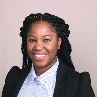 A smiling woman with braided hair wearing a blazer and a button-down shirt.