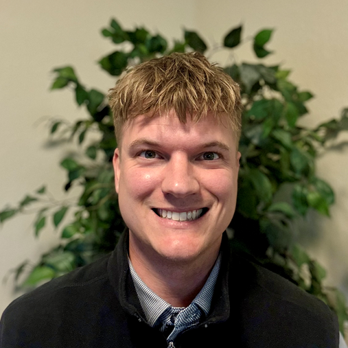 Smiling man with blonde hair and a black vest.