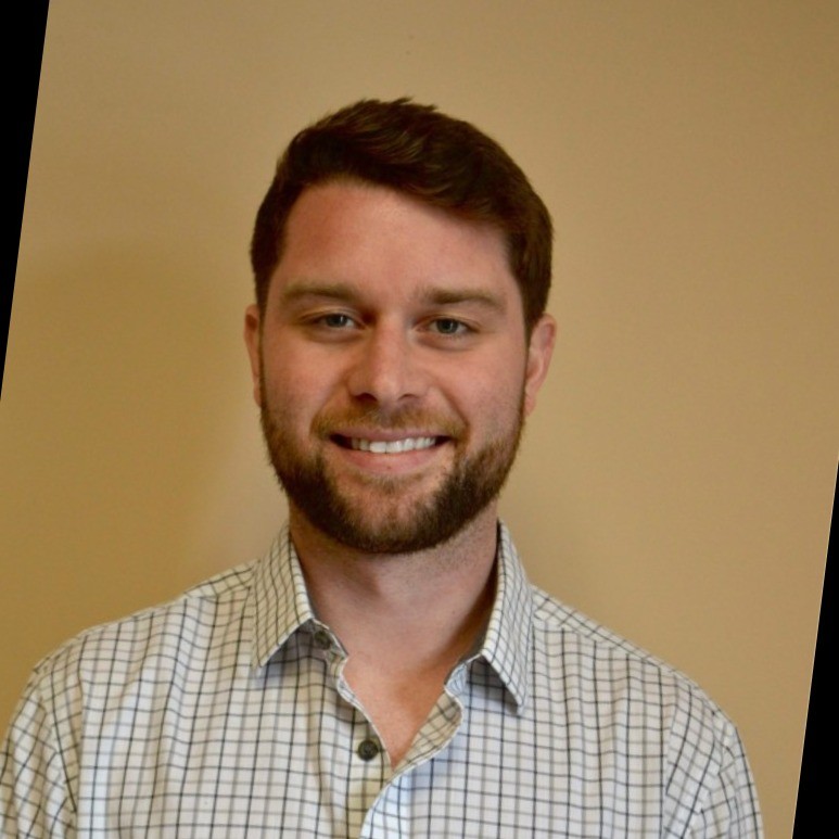 Man with beard and checkered shirt, smiling.