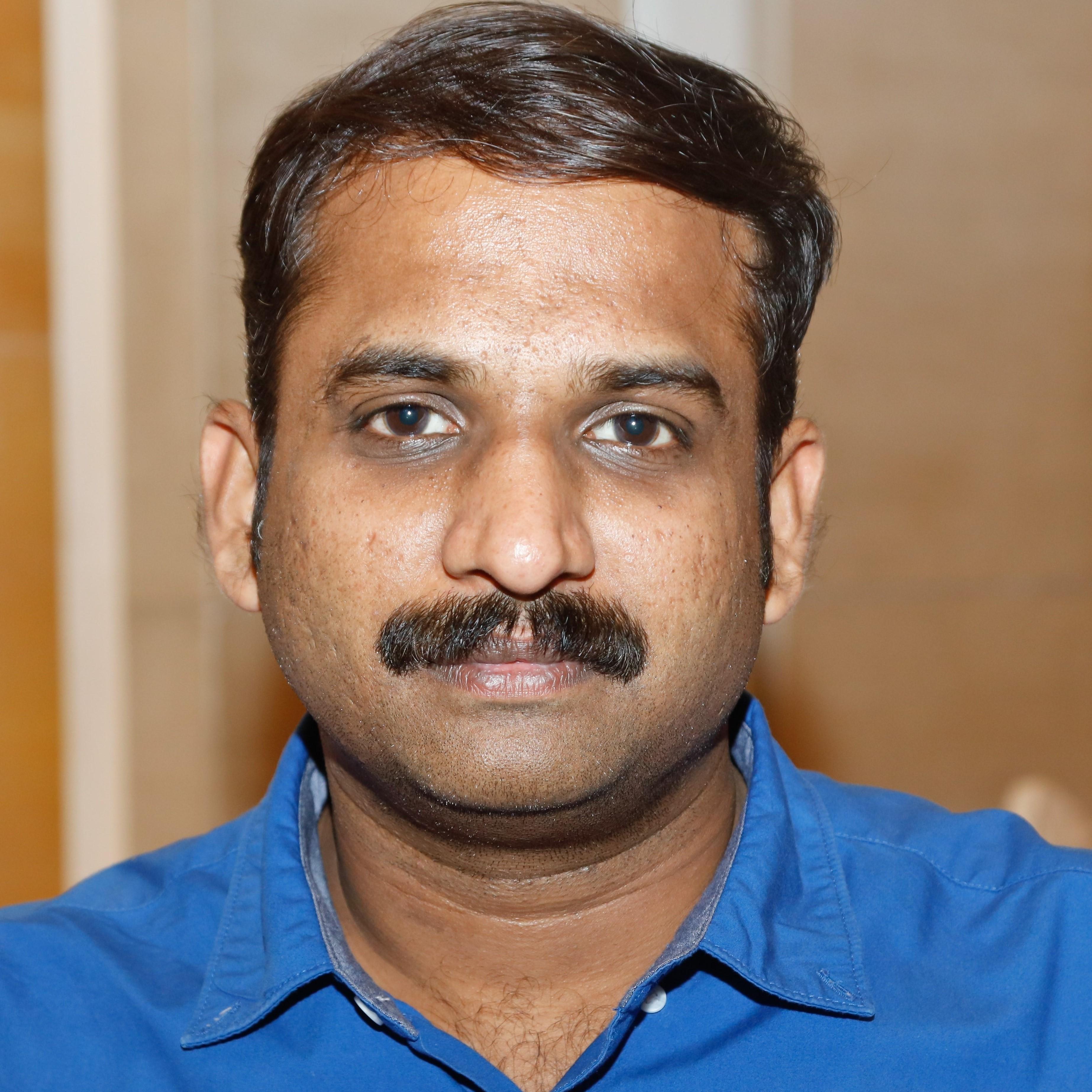 Man with mustache wearing a blue collared shirt.