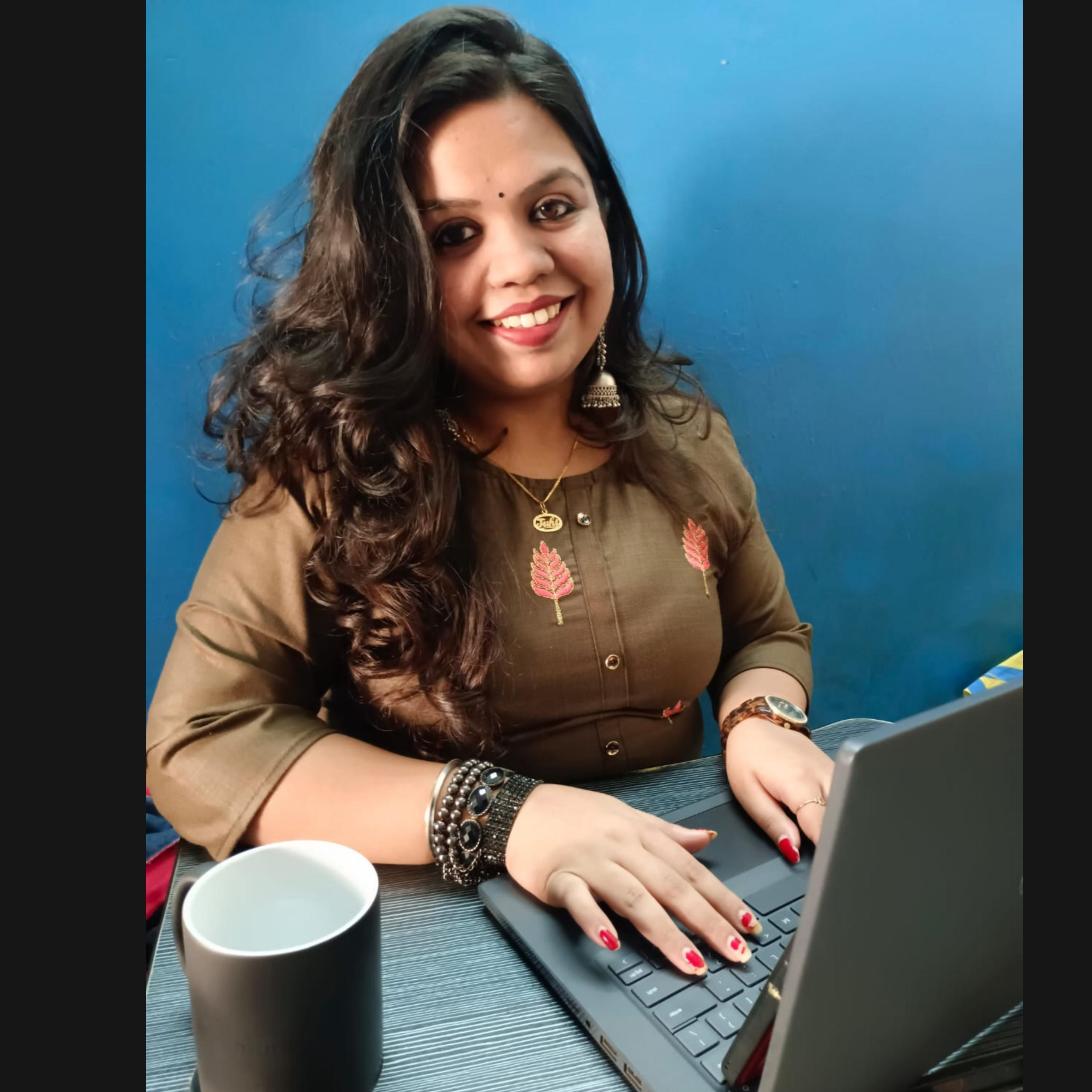 Woman smiling, working on laptop. Wearing earrings and a necklace.