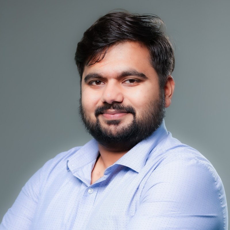 Close-up of a smiling man with a beard, wearing a blue shirt, gray background.