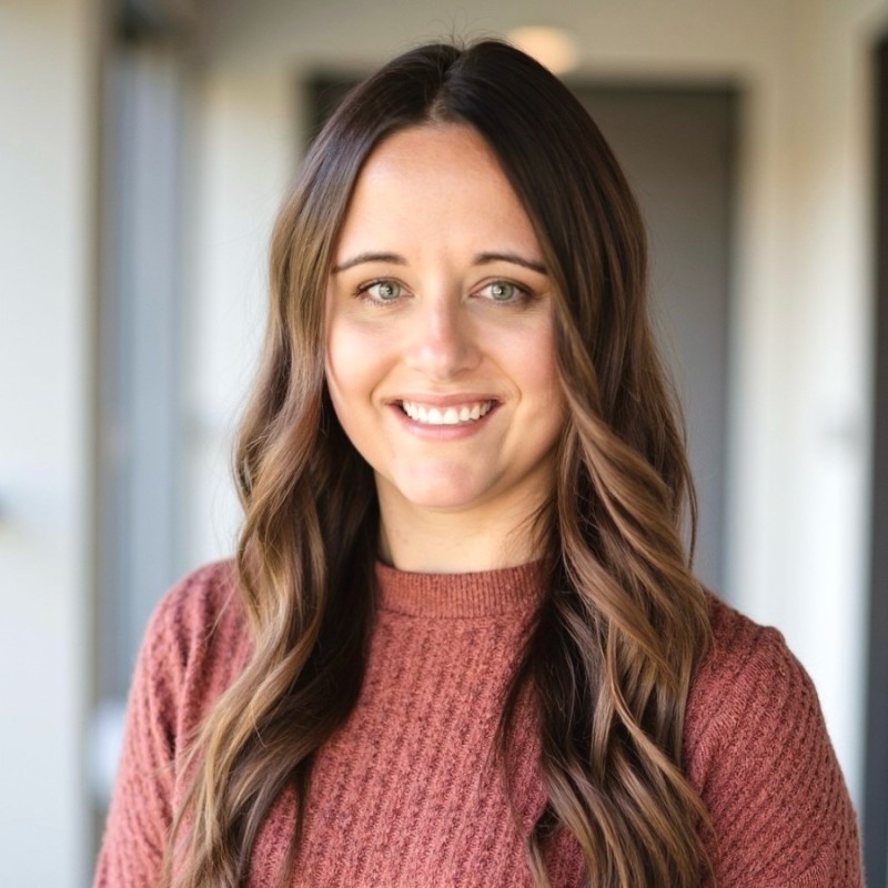 Woman with long brown wavy hair smiling, wearing a red sweater.