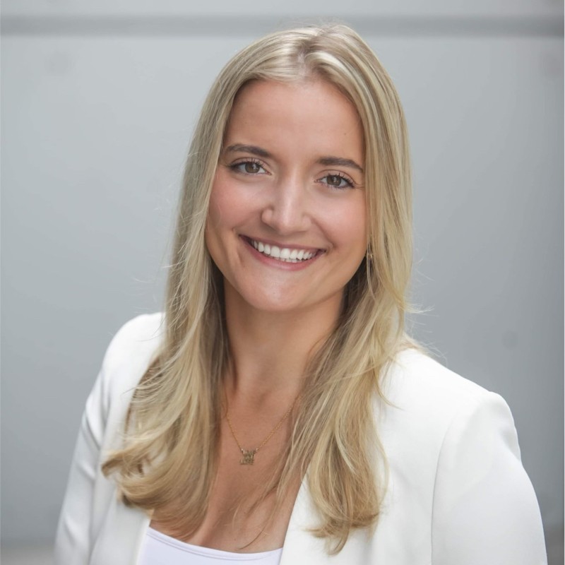 Blonde woman wearing a white blazer smiling at the camera.